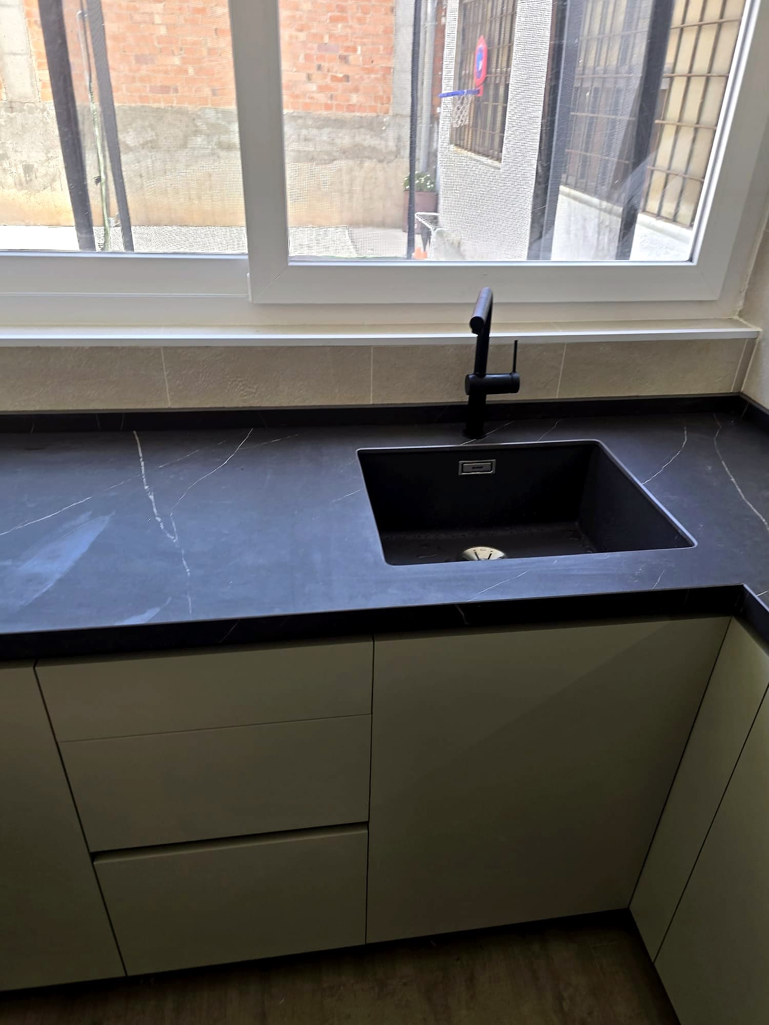 Fregadero negro bajo encimera oscura veteada con grifo negro, frente a una ventana