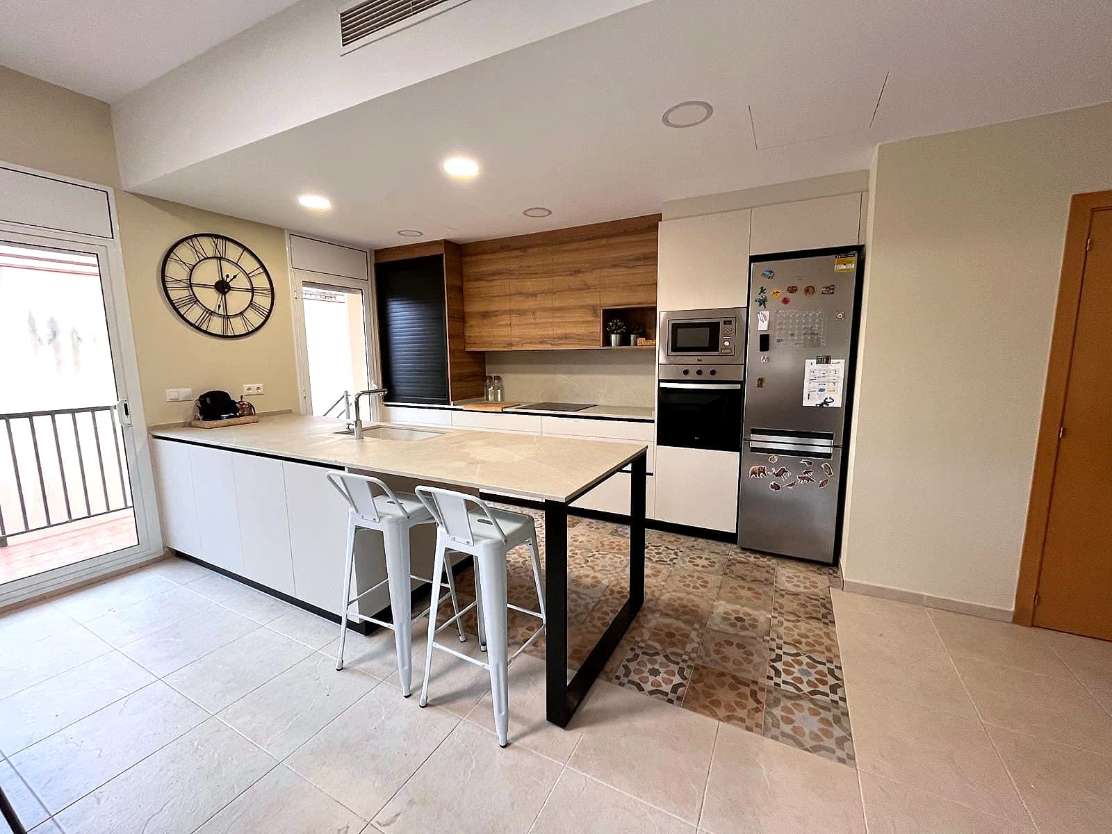 Cocina blanca y madera con isla, barra de estructura negra y suelo hidráulico de colores cálidos