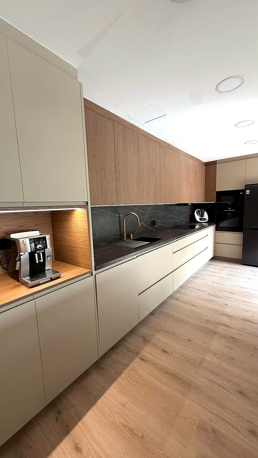Frente de cocina con nicho iluminado para la cafetera, muebles altos de madera y frontal de piedra oscura