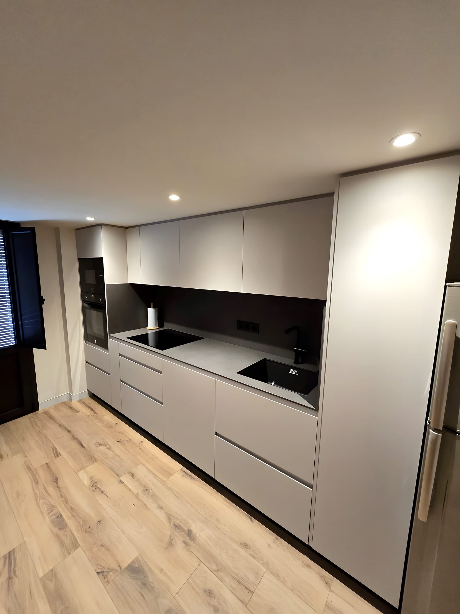 Cocina gris claro con frontal oscuro y gran isla antracita en cascada sobre suelo de madera