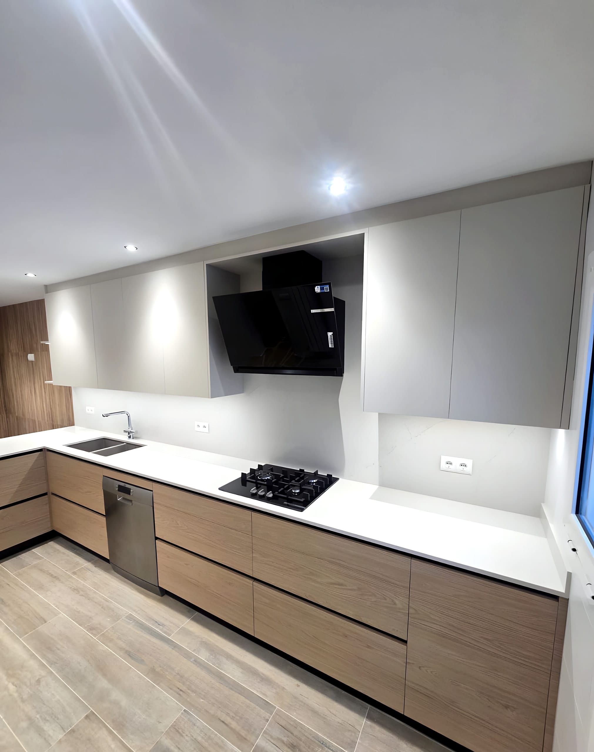 Cocina en U con bajos en madera clara, altos gris claro, encimera blanca en cascada y campana negra