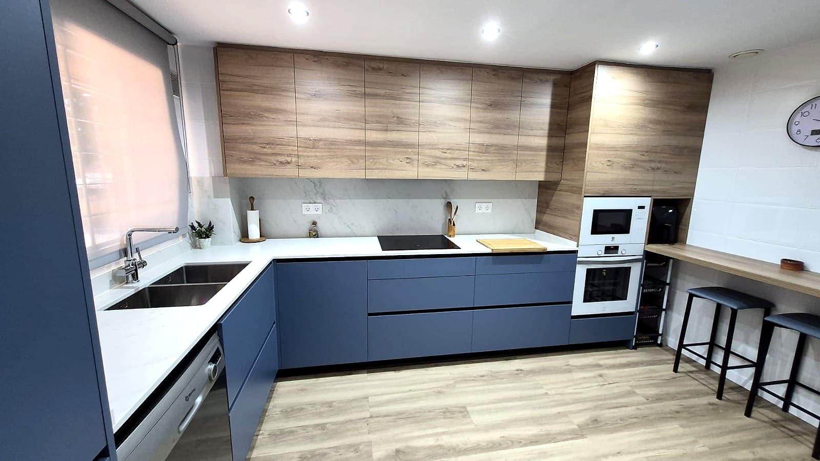 Cocina azul y roble en U con barra de desayuno y taburetes junto a la ventana