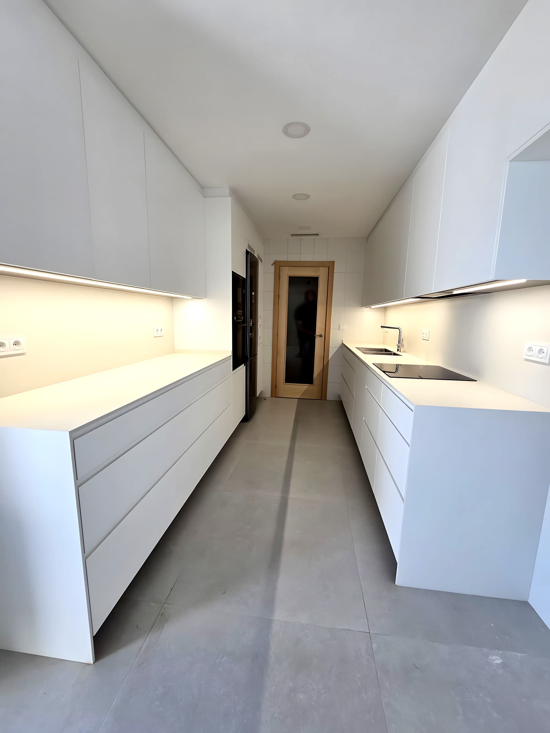 Cocina en paralelo totalmente blanca con muebles hasta el techo y luz lineal bajo los muebles altos