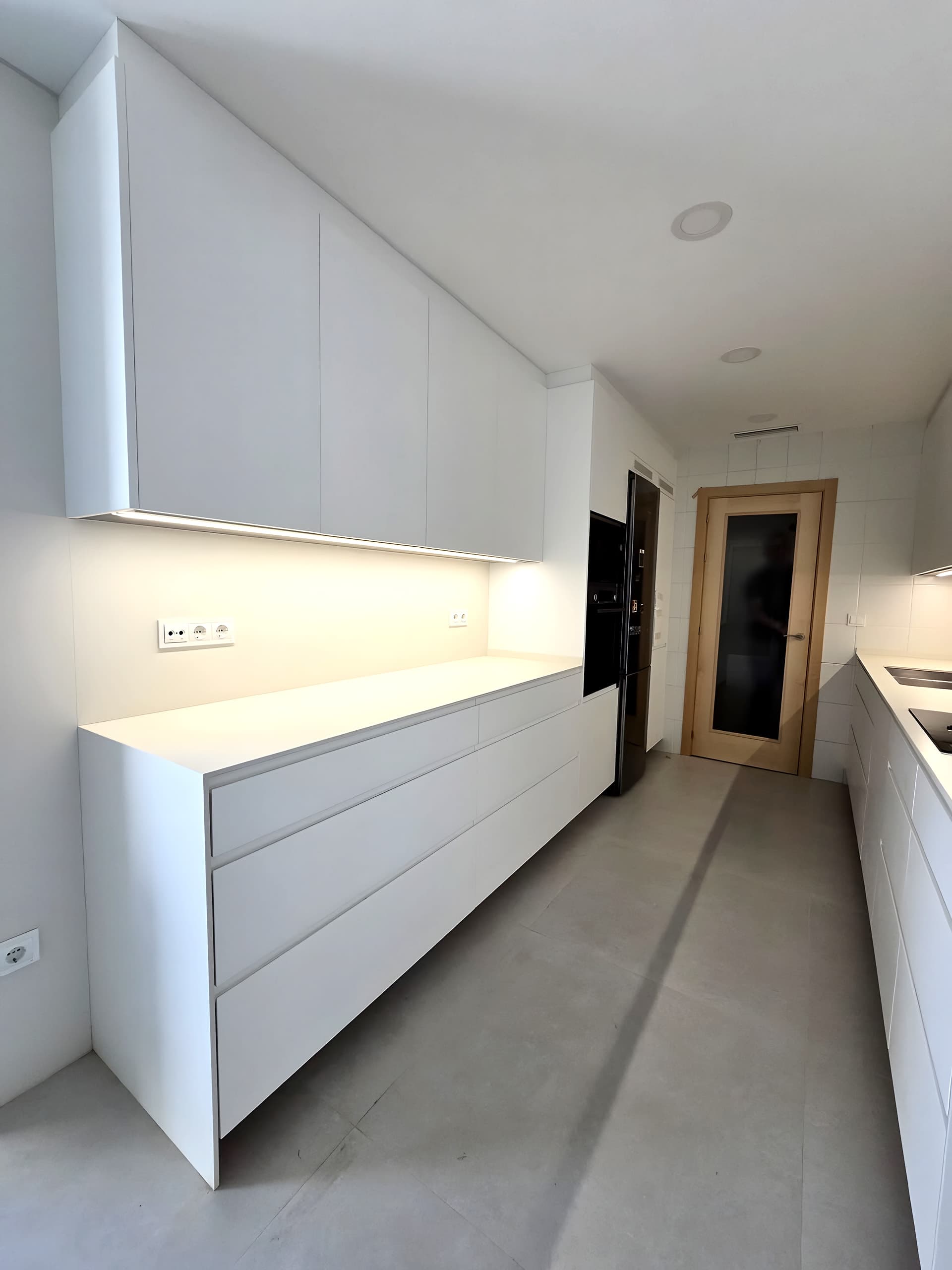 Frente blanco de cajones con encimera continua y luz lineal cálida bajo los muebles altos