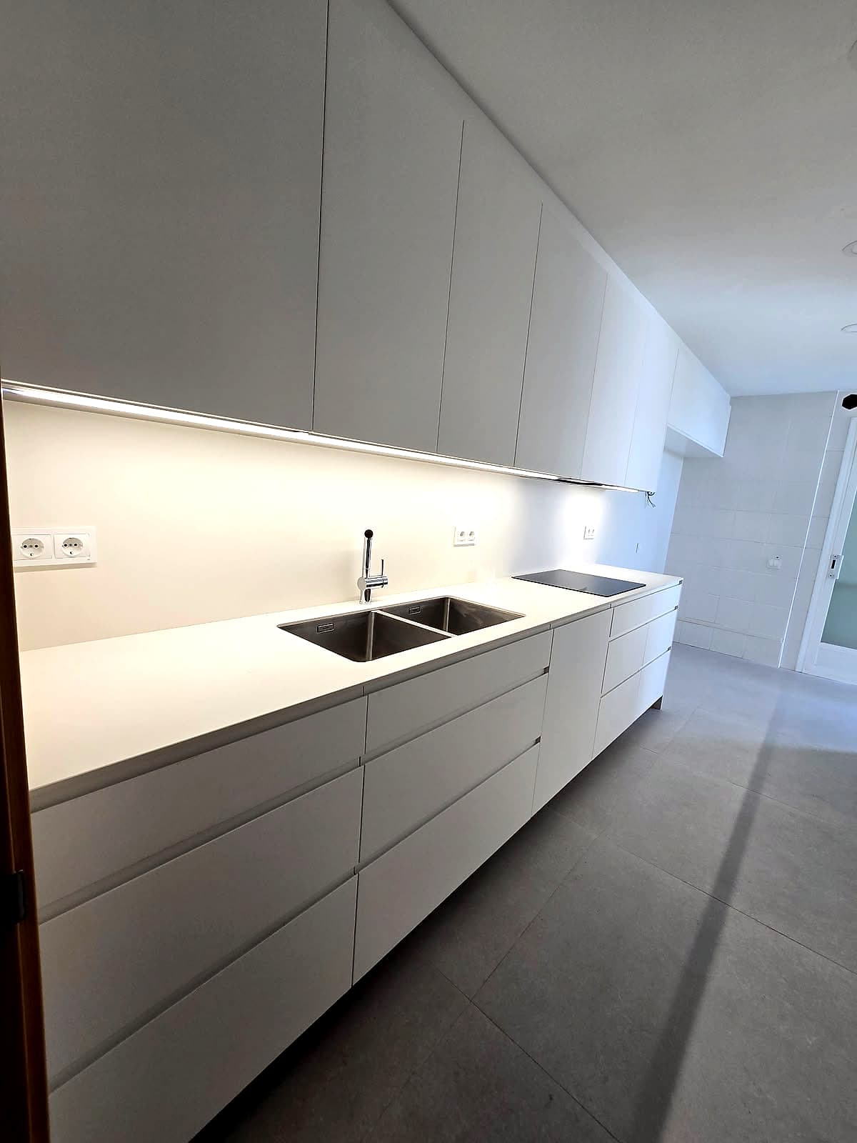 Encimera blanca con fregadero doble de acero, grifo cromado y placa, bajo muebles altos blancos