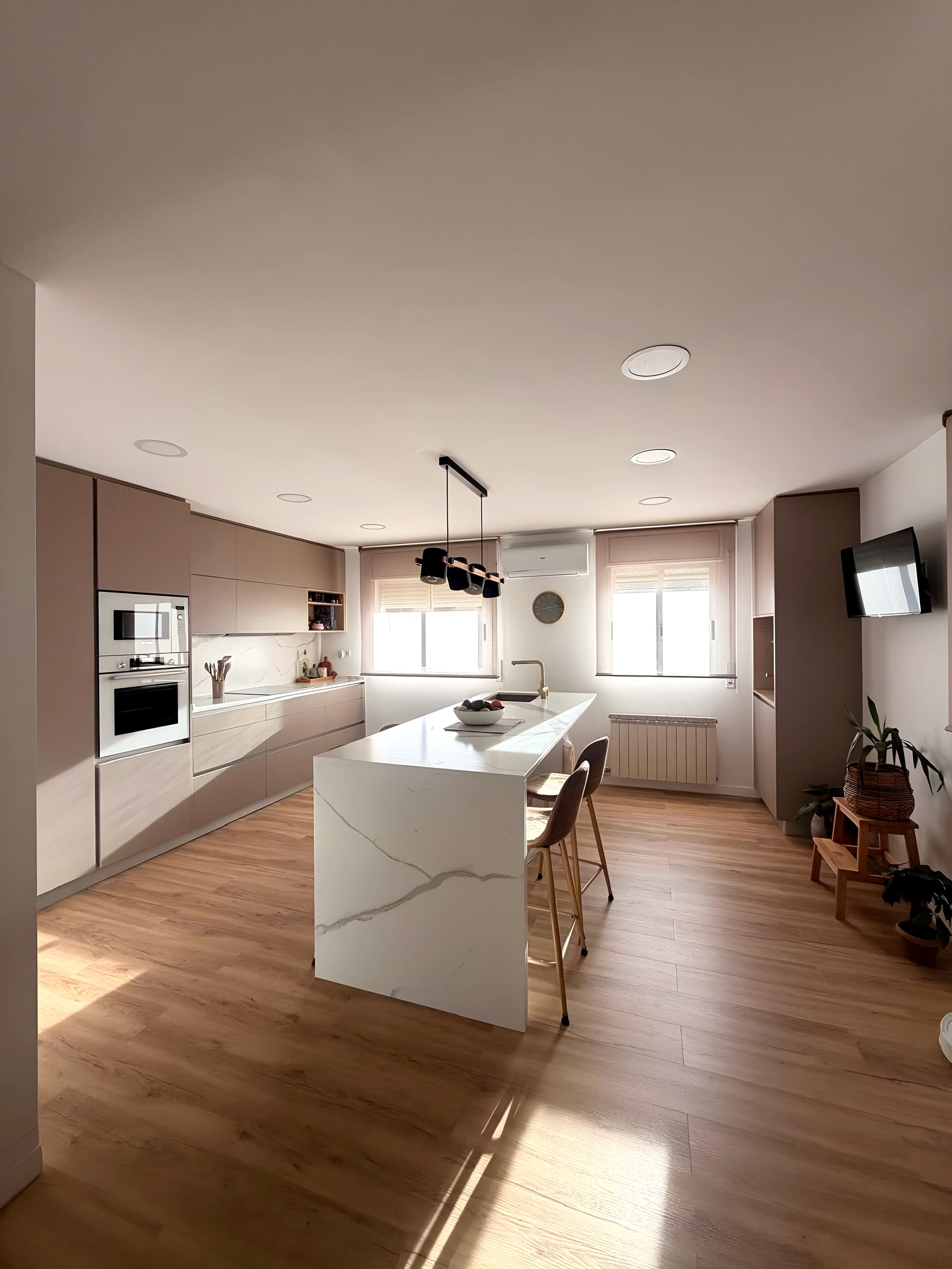 Cocina luminosa en tonos topo con isla blanca veteada en cascada, taburetes y lámpara negra de focos