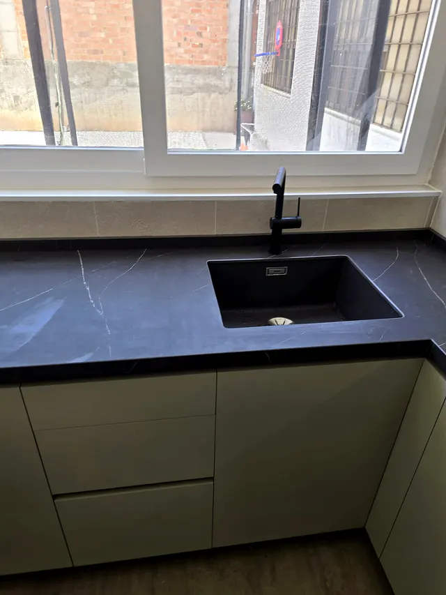 Fregadero negro bajo encimera oscura veteada con grifo negro, frente a una ventana