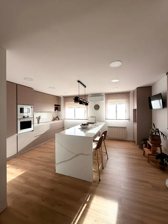 Cocina luminosa en tonos topo con isla blanca veteada en cascada, taburetes y lámpara negra de focos