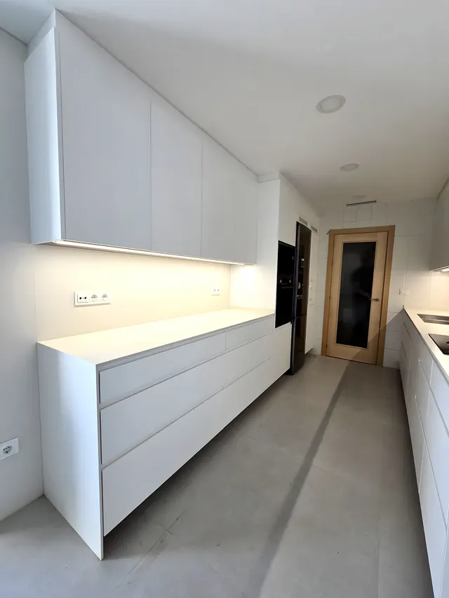 Frente blanco de cajones con encimera continua y luz lineal cálida bajo los muebles altos