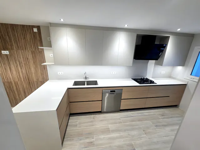 Cocina en U con bajos en madera clara, altos gris claro, encimera blanca en cascada y campana negra