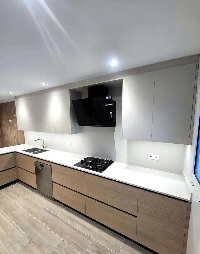 Frente de cocina con bajos de madera clara, placa de gas, campana de cristal negro y altos gris claro