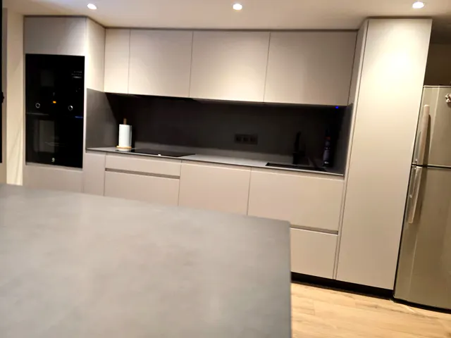 Vista frontal de la cocina gris claro con horno y microondas negros en columna y frontal oscuro