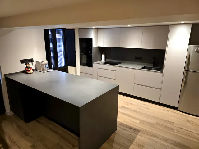 Cocina gris claro con frontal oscuro y gran isla antracita en cascada sobre suelo de madera