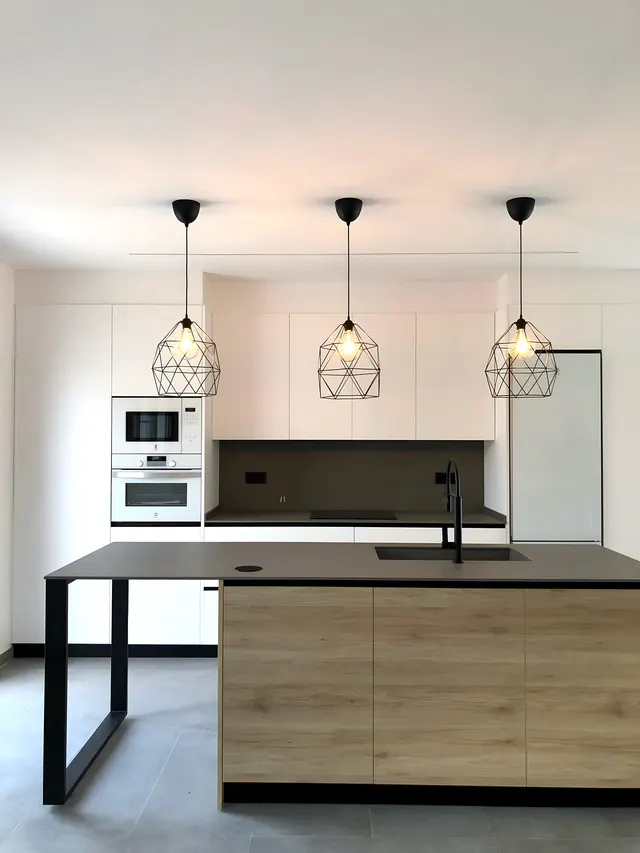 Cocina blanca con isla de frente en roble, encimera oscura, pata de acero negro y tres lámparas geométricas