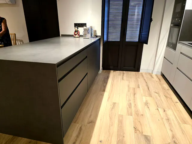 Lateral de la isla antracita con cajones de gran formato y uñero, junto a una puerta con contraventanas
