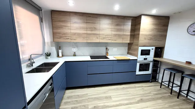 Cocina azul y roble en U con barra de desayuno y taburetes junto a la ventana